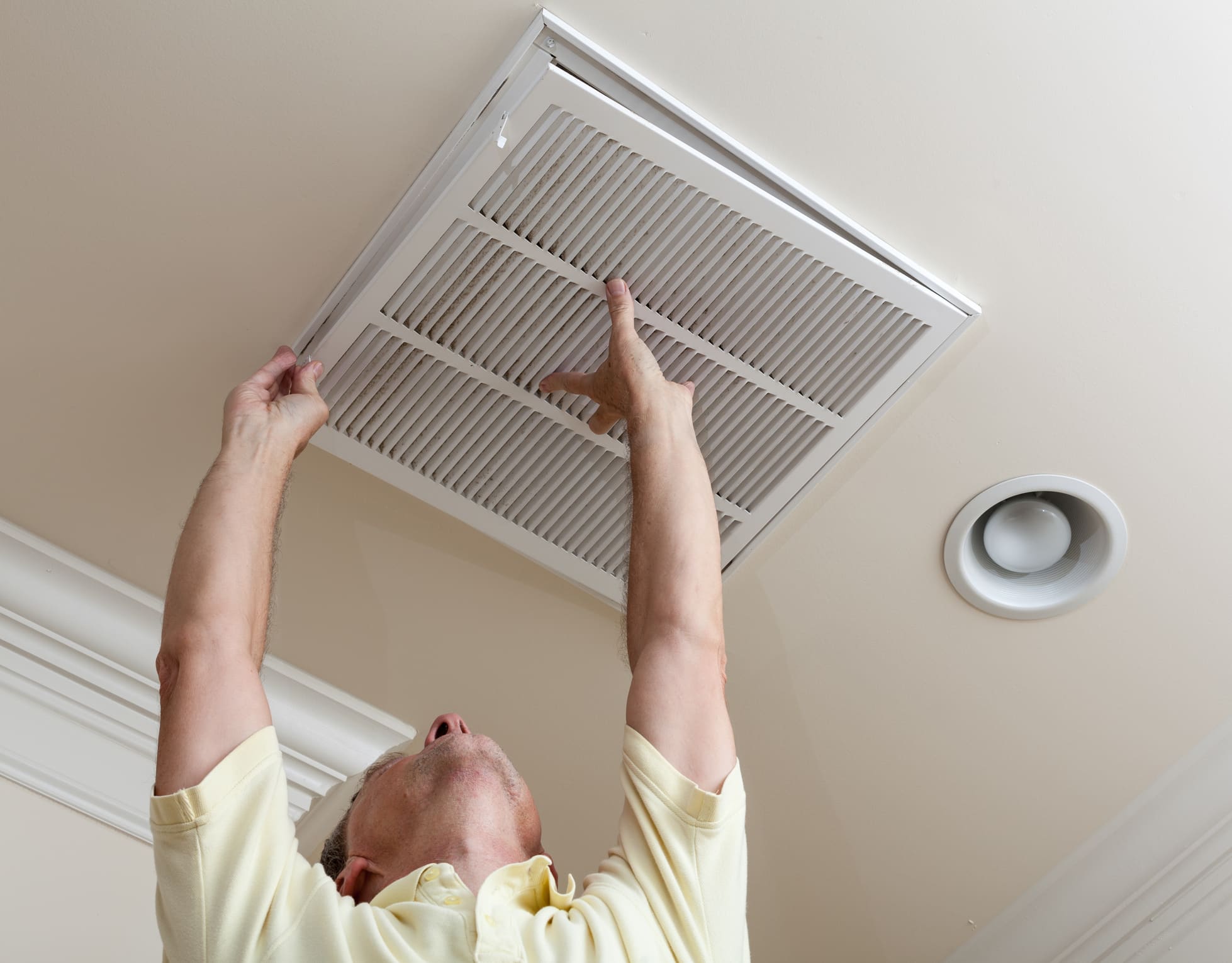 A man looking up opening air conditioning filter in ceiling, HVAC Performance.