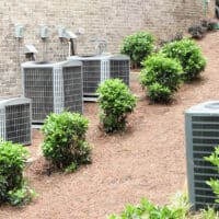 Multiple residential air conditioning units in a landscaped area of a home contribute to the HVAC load, impacting energy efficiency and performance.